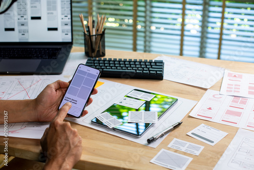 UX UI designer testing prototype on a phone, working on wireframes for a website and mobile app prototype, in concept of website and mobile application design concept.