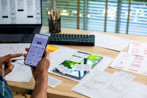 UX UI designer testing prototype on a phone, working on wireframes for a website and mobile app prototype, in concept of website and mobile application design concept.