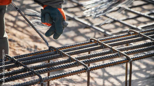 Картината върху платно A worker is tying steel bars together to form reinforcement for a concrete foundation in a construction area