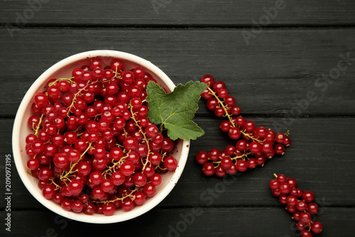Red currants on white plate on black wooden background. Fresh and vibrant food photography for healthy eating.