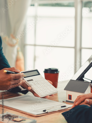Real estate agent pointing at contract document on clipboard, explaining terms to client during home loan insurance meeting.