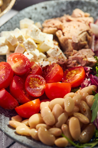 Healthy Mediterranean salad with canned tuna, white beans, feta cheese, cherry tomatoes, and greens on a stone plate.