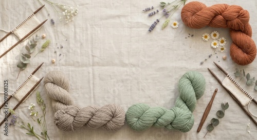 Soft natural yarn skeins in pastel and earthy tones arranged with wooden knitting needles, eucalyptus leaves and wildflowers on linen background. Cozy handmade craft concept.

