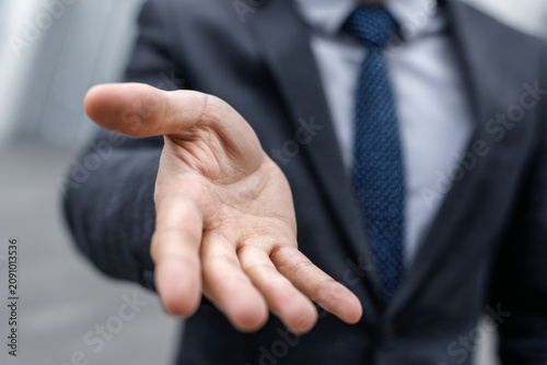 Close up of businessperson hand extended forward in gesture of offering or handshake, dressed in suit and tie