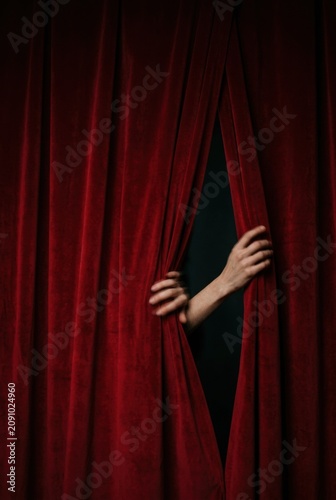Red velvet stage curtains filling the frame as hands emerge to part the fabric for a theatrical performance, suspenseful premiere reveal imagery with copy space