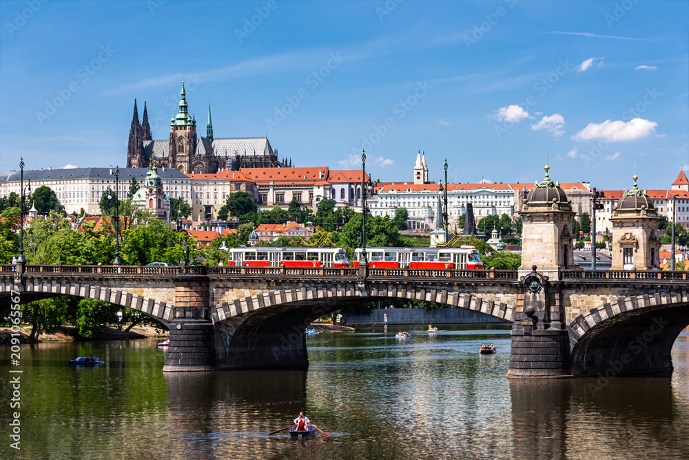 Obraz premium Prague Castle and St Vitus Cathedral overlook the Vltava River in a bright summer cityscape with bridges and historic architecture in the Czech capital.