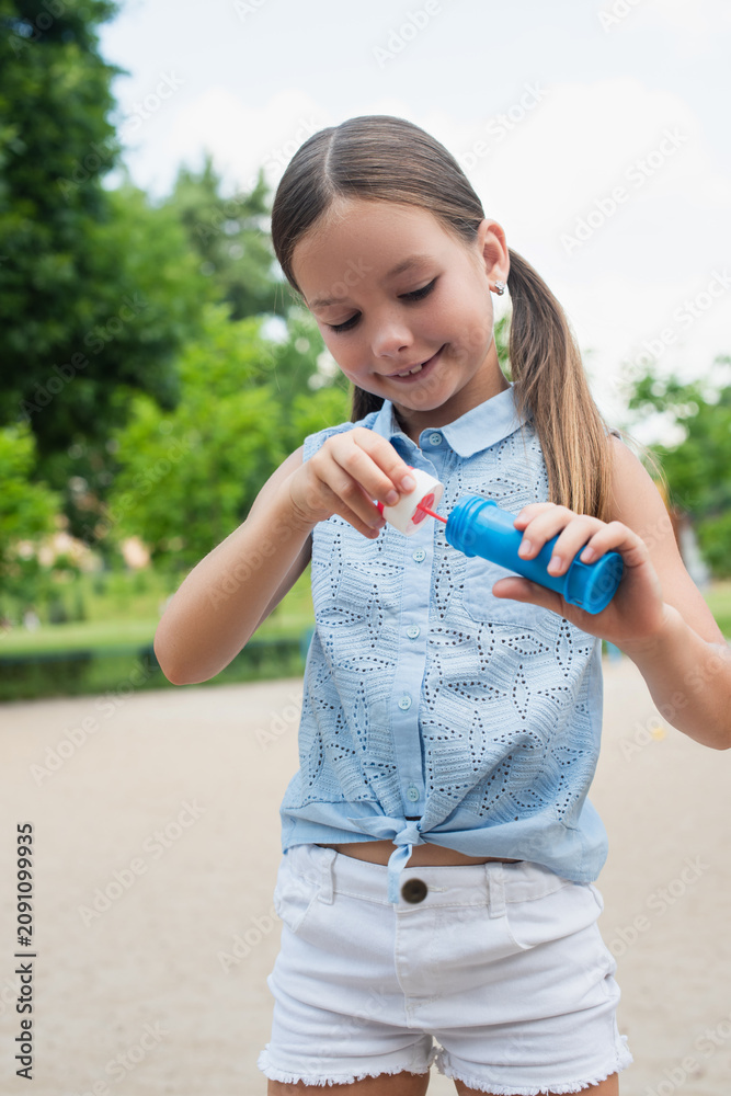 Naklejka premium Joyful moments of childhood as a little girl plays with bubbles in a sunny park setting