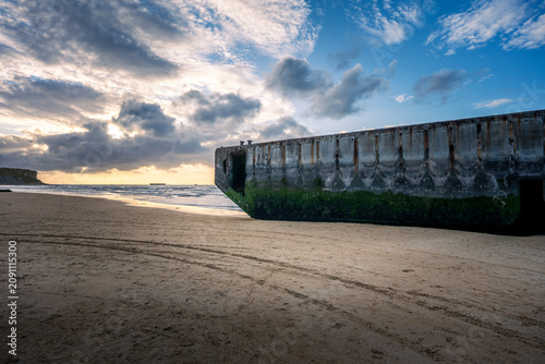 Historical World War II concrete Mulberry harbour caisson on Gold Beach at Arromanches-les-Bains in Normandy, France, during sunset.
