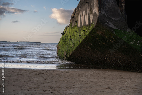 Historical World War II concrete Mulberry harbour caisson on Gold Beach at Arromanches-les-Bains in Normandy, France, during sunset.