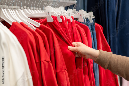 Female hand choosing bright red hoodie on clothing rack in fashion store