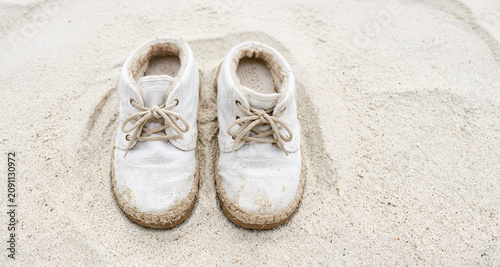 Immagine con primo piano di un vecchio paio di scarpe in tela bianca lasciate su una superficie di fine sabbia bianca