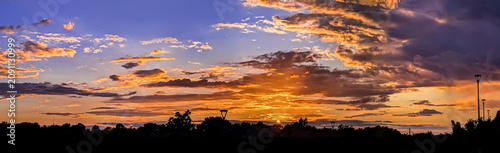 Vibrant sunset sky with orange clouds background. Beautiful dramatic sunset sky colorful clouds in shades violet, golden, yellow and red brown. High resolution gold hour sky. Dramatic scene of the end