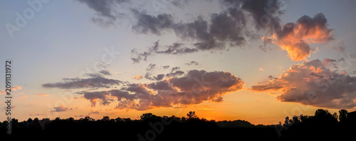 Serene hot summer sunset above town roofs across a quiet reservoir with warm golden tones and smooth clouds, creating a tranquil and atmospheric landscape.