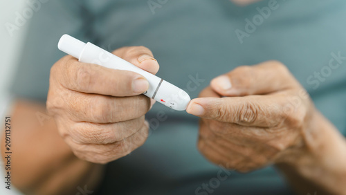Photos Close-up of a senior adult preparing a finger prick with a lancet device for blood glucose monitoring at home