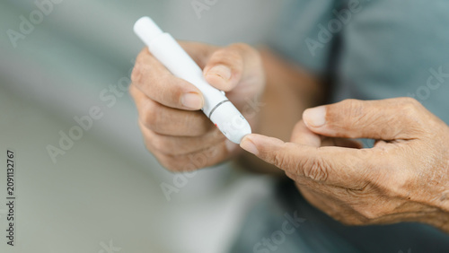 Obraz na plátně Close-up of a senior adult using a lancet device for finger prick blood glucose testing at home