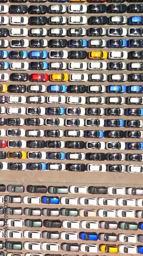 A drone rises above a vast terminal where thousands of new cars sit neatly parked