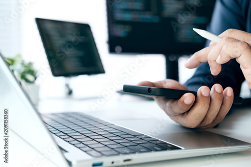 Software Developer Testing Mobile Application Interface on Smartphone, Reviewing Source Code on Laptop for Cross Platform App Development, Debugging, Quality Assurance, User Experience Validation
