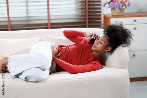 Fotografie Young woman suffering from abdominal pain lying on sofa, telephoning doctor for