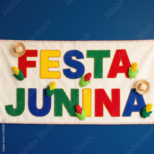 Bright felt letters spell Festa Junina with decorative corn, hats, and space for text. Festive Brazilian June party banner in primary colors on blue background.