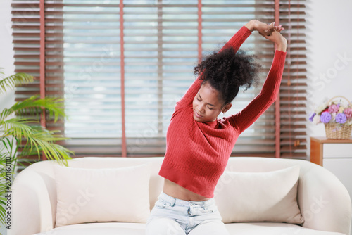 Young black woman stretching arms upward, relaxing at home, performing gentle exercise for health and well-being, finding comfort in a peaceful household environment