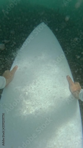 VERTICAL, FPV, SLOW MOTION: Surfer pushes white surfboard down during a duck dive beneath a breaking wave. Practical technique for returning to the lineup while surfing in tropical Mentawai Islands.