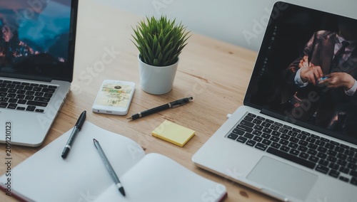 Two Laptops and a Notebook on a Desk With a Plant and Stationary in a Workspa...