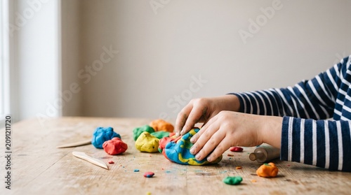 Childs hands playing with colorful modeling clay on a wooden table