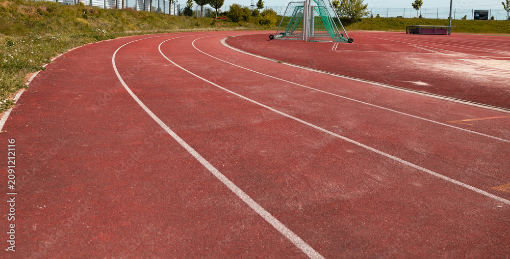 Fototapeta premium Close shot of a red tartan track with white markings on an outdoor sports field. Track for training and competitions. Leisure activity, sports facility, soccer field.
