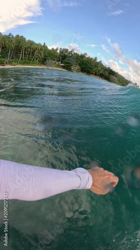 VERTICAL, FPV: Smooth surfing and splashing turns on a peeling wave near tropical coastline. Spraying water, sun, turquoise sea and riding surfboard on long glassy waves at remote Indonesian surf spot