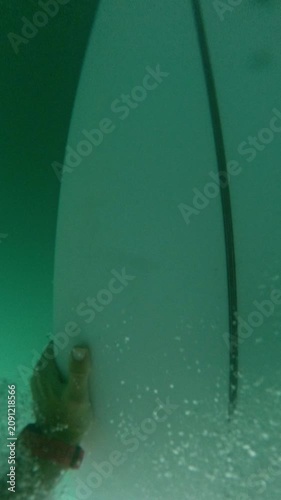 VERTICAL, FPV, SLOW MOTION: Surfer makes duck dive in front of approaching wave. Surfboard slices underwater, surrounded by bubbles and turquoise water. Rider paddles back out through breaking waves