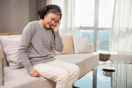 Foto Elderly woman feeling dizzy and unwell while sitting on sofa at home