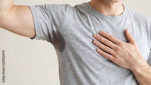 Man showing armpit with sweat stain on grey t-shirt. concept of hyperhidrosis and excessive sweating.