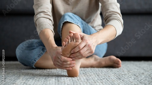 Woman sitting on floor holding painful foot massaging arch to relieve soreness and discomfort.