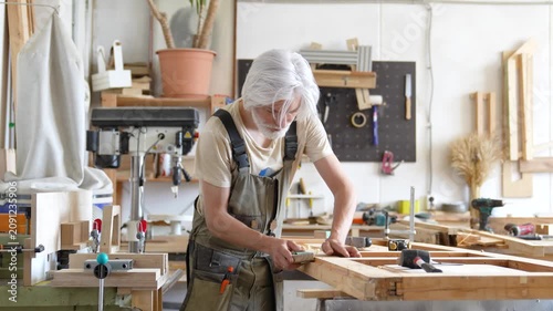 Woodworking and modern restoration workshop settings, professional passionate restorer repairing window frame, precise man crafter sanding frame surface with sandpaper and adjusting with chisel tool.