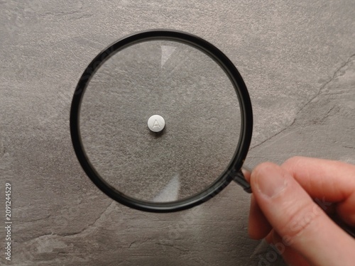 Foto Close up of a white pill with a letter A viewed through a magnifying glass on a gray table