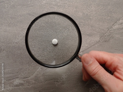 Bild auf Leinwand Close up of a white pill with a letter A viewed through a magnifying glass on a gray table