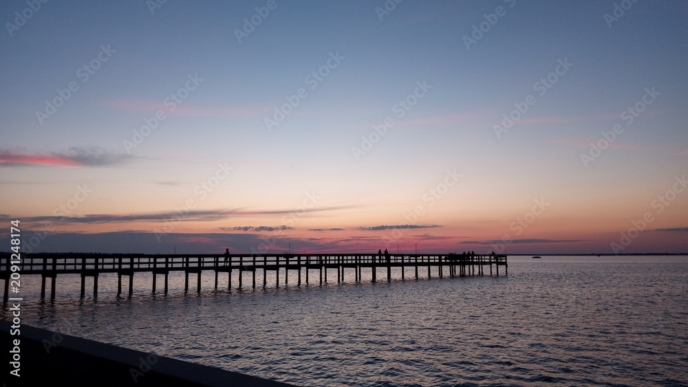 Obraz premium Wooden pier extending into calm water at colorful twilight sunset