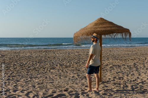 Tableau sur toile Hispanic man enjoying sunny beach beside straw umbrella