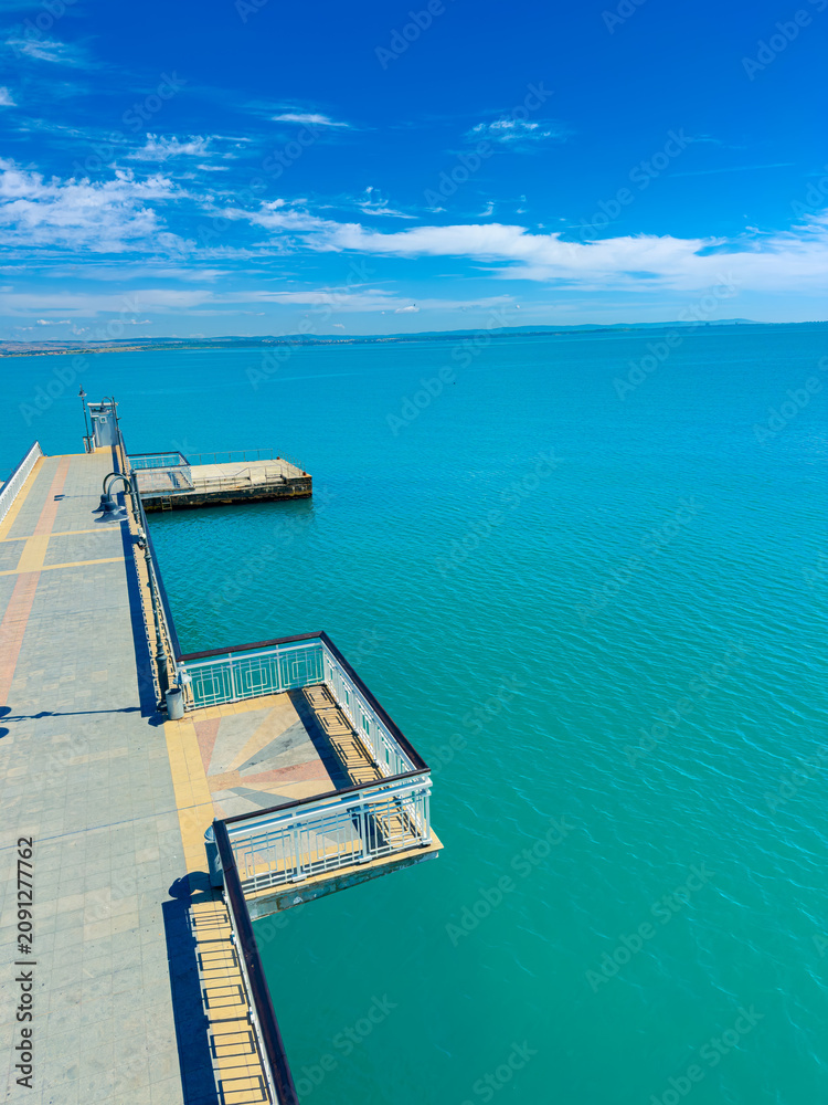 Fototapeta premium View of a long pier extending over calm blue waters under a clear sky with a few clouds during daytime at a coastal location