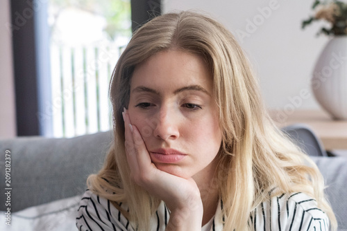 Tableau sur toile Young woman sitting on a couch at home looking pensive and bored, resting her face on her hand and appearing thoughtful, lonely, or melancholic in a casual living room setting