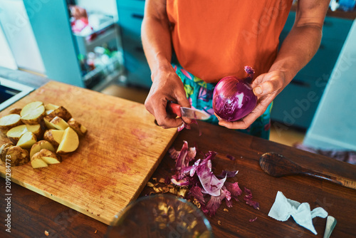 Woman preparing dinner - peeling onion with potatoes on the board