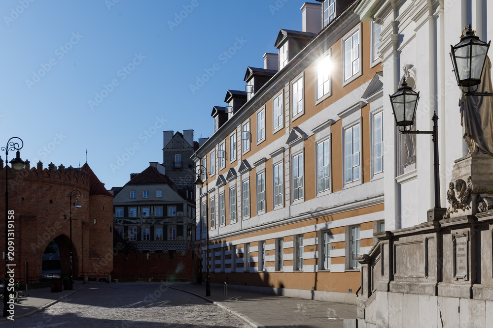 Fototapeta premium Empty cobblestone street near the historic brick barbican in Warsaw, Poland during a bright and sunny early morning.