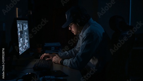 Man Works at Computer in Dark Office Late at Night With Shadows in Background