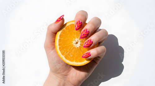 Woman hand with colorful chevron nail art holding a fresh orange slice on white background.