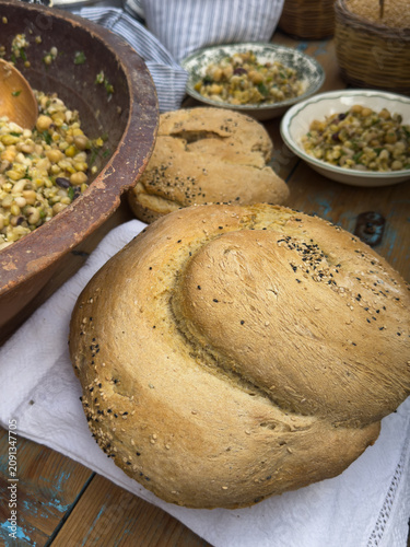 Vertical shot of rustic table setting with traditional Cretan eftazymo bread loaves and ceramic bowls filled with fotokollyva, a festive legume salad from Crete, Greece.