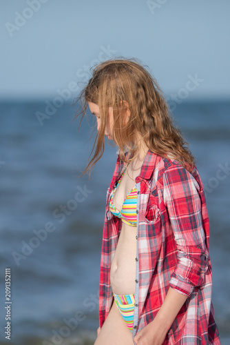 Girl in red plaid shirt standing by sea waves on beach.
