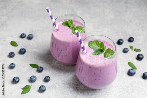 Tasty smoothie in glasses, fresh blueberries and mint on grey table, closeup