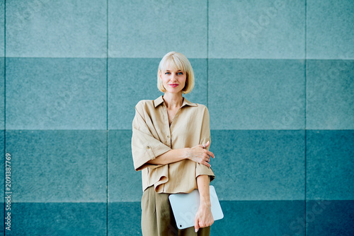 Canvastavla Young blonde female professional holding digital tablet, smiling, standing confi