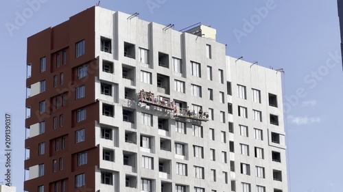Workers on scaffolding are seen cleaning the windows of a modern apartment building, showcasing the ongoing maintenance of the structure in an urban environment with clear blue skies