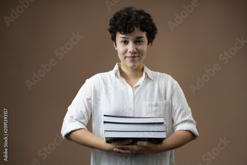 Beautiful young woman holding a stack of books. Horizontal studio portrait with copy space on brown background. Ideal for university student content, adult education and reading habit.
